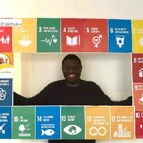 Andrew står foran en plakat med de SDG mål for bæredygtig udvikling, der fremmer regenerativ praksis og organisationer for bæredygtig udvikling.