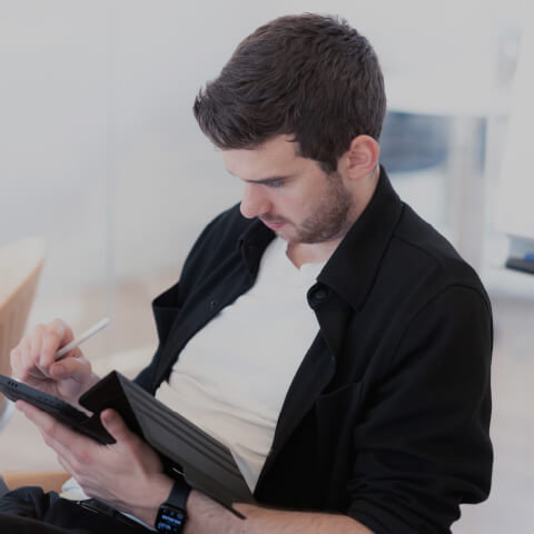 Sebastian sidder på en stol og skriver på en tablet som en del af sin lederrolle i organisationsudvikling.