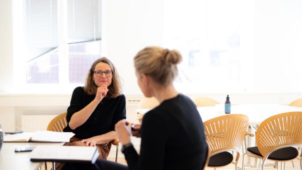 To kvinder sidder ved et bord i et mødelokale og diskuterer ledelse (ledelse) og organisationsudvikling (organisationsudvikling).