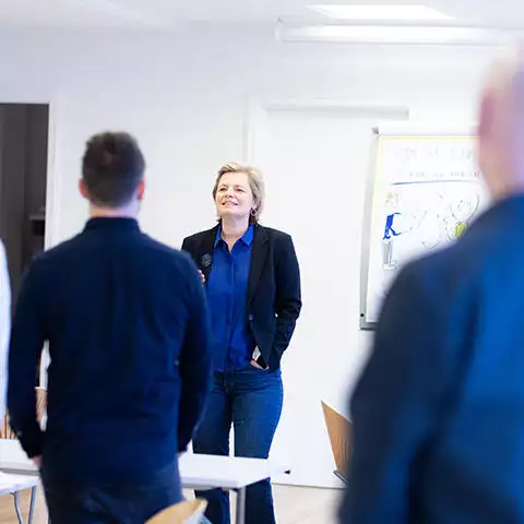 En frisættende gruppe mennesker engageret i regenerativ organisationsudvikling står i promentums eventlokale imens Ann Graugaard taler.