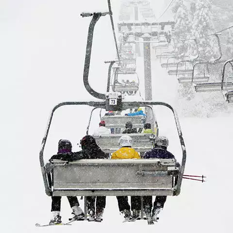 En gruppe mennesker på en skilift på vej op til toppen af en bakke.