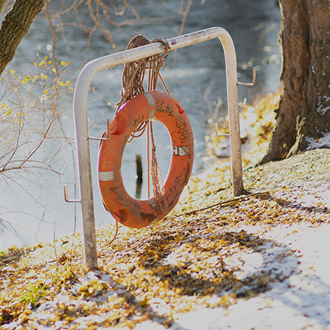 En gammel overmalet orange redningskrans på en metalstang nør vandet.