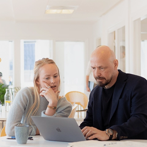 En mand og en kvinde sidder ved et bord og ser på en bærbar computer i promentums lokaler.